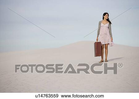 A young woman walking in the desert carrying a suitcase View Large Photo Image Stock Photo - A young woman walking in the desert carrying a suitcase. Fotosearch