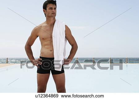 Stock Photo - A young man standing by a swimming pool. Fotosearch