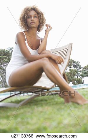 Stock Photograph - A young woman sitting on a sun lounger. Fotosearch
