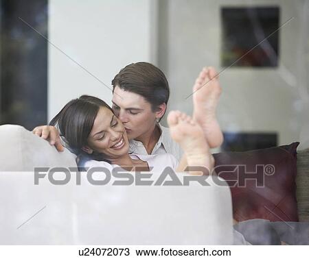 Stock Image - A young couple kissing on the sofa. Fotosearch