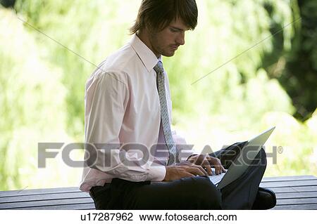 Stock Image - A businessman using a laptop in a garden. Fotosearch