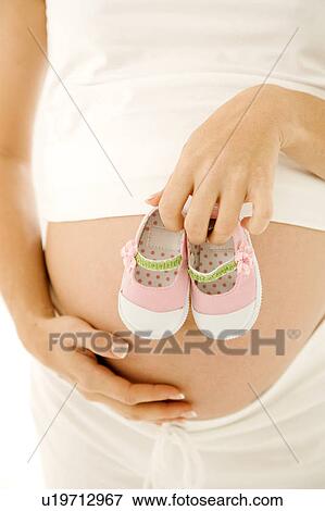 Stock Photo - A pregnant woman holding a pair of baby shoes. Fotosearch