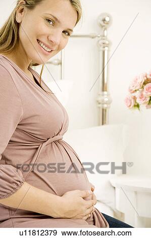 Stock Photo - A pregnant woman holding her bump. Fotosearch