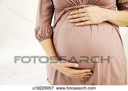 Stock Photo - A pregnant woman holding her bump. Fotosearch