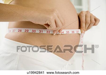 Stock Image - A pregnant woman measuring her waist. Fotosearch