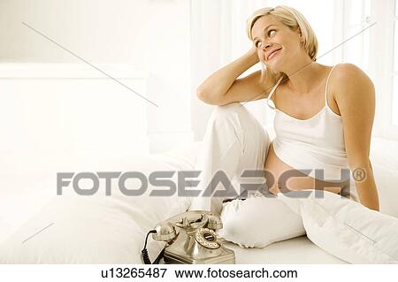Stock Photo - A pregnant woman sitting by the telephone. Fotosearch