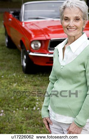 Stock Image - A senior woman standing by a sports car. Fotosearch