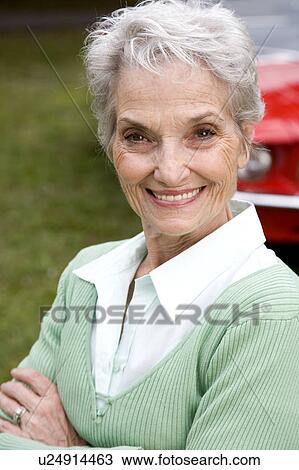 Stock Image - A senior woman standing by a sports car. Fotosearch