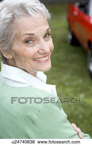 Stock Photo - A senior woman standing by a sports car. Fotosearch