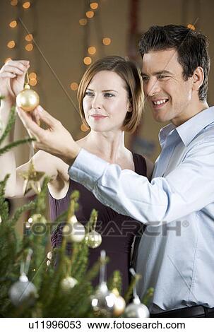 A couple hanging decorations on a Christmas tree View Large Photo Image Stock Image - A couple hanging decorations on a Christmas tree. Fotosearch