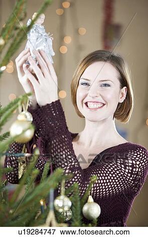 Stock Photo - A woman putting the fairy on top of the Christmas tree. Fotosearch
