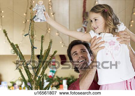 A father lifting his daughter to place the fairy on top of the Christmas tree View Large Photo Image Stock Photo - A father lifting his daughter to place the fairy on top of the Christmas tree. Fotosearch