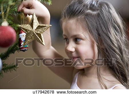 Stock Photo - A young girl putting a decoration on a Christmas tree. Fotosearch