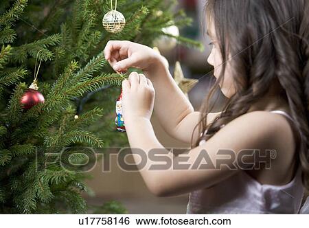 Stock Photograph - A young girl putting a decoration on a Christmas tree. Fotosearch