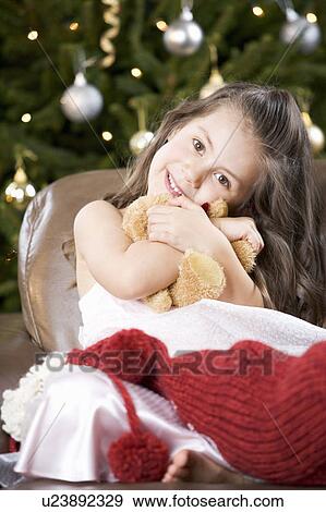 Stock Photo - A young girl with a Christmas stocking hugging her teddy bear. Fotosearch