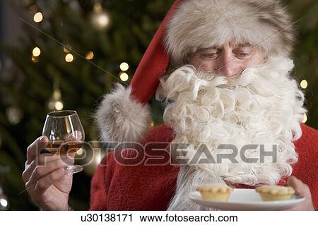 Stock Image - Father christmas / santa Claus eating mince pies with a glass of brandy. Fotosearch