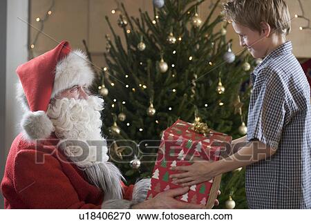 Father christmas / santa Claus offering a present to a young boy View Large Photo Image Stock Image - Father christmas / santa Claus offering a present to a young boy. Fotosearch