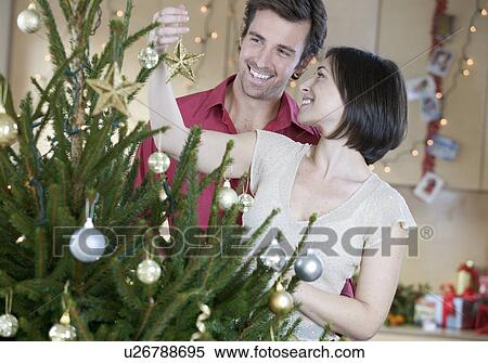 A couple decorating the Christmas tree View Large Photo Image Stock Photography - A couple decorating the Christmas tree. Fotosearch