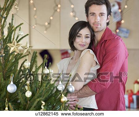 A couple standing by the Christmas tree View Large Photo Image Stock Photography - A couple standing by the Christmas tree. Fotosearch