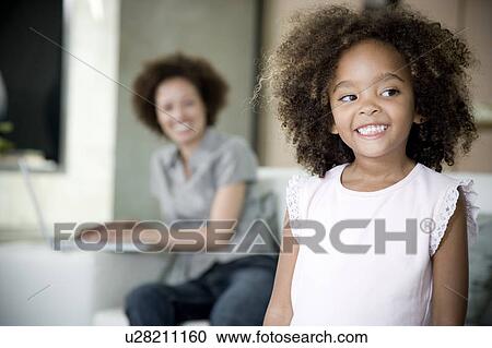 Little girl at home smiling, mother in background working on laptop View Large Photo Image Stock Image - Little girl at home smiling, mother in background working on laptop. Fotosearch
