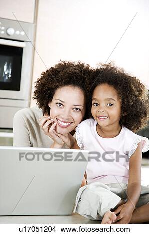 Picture - Mother and daughter with laptop in the kitchen at home. Fotosearch
