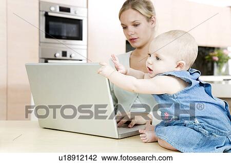 Mother typing on a laptop at home with baby beside her View Large Photo Image Stock Image - Mother typing on a laptop at home with baby beside her. Fotosearch