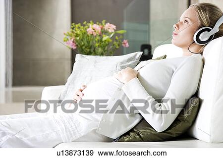 Stock Photo - Pregnant woman relaxing whilst listening to music on headphones. Fotosearch