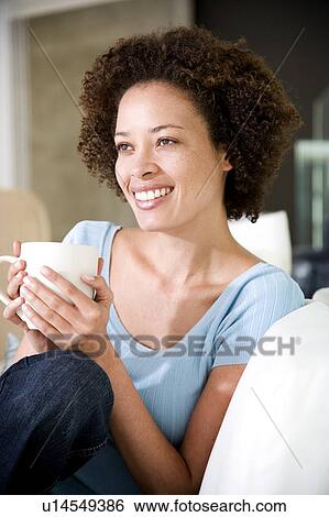 Woman sitting on sofa drinking a cup of tea or coffee View Large Photo Image Stock Photograph - Woman sitting on sofa drinking a cup of tea or coffee. Fotosearch