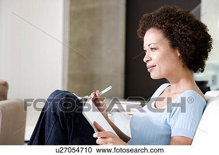 Stock Image - Woman writing a diary or journal, relaxing at home. Fotosearch