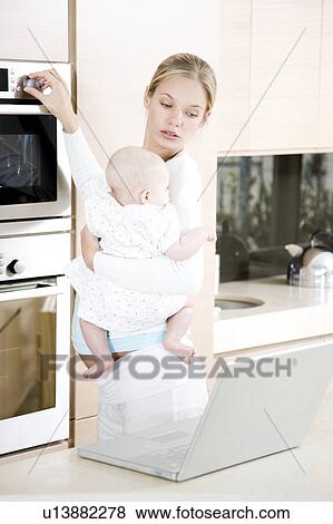 Young mother multi-tasking - holding baby, cooking dinner and looking at laptop View Large Photo Image Stock Photo - Young mother multi-tasking - holding baby, cooking dinner and looking at laptop. Fotosearch