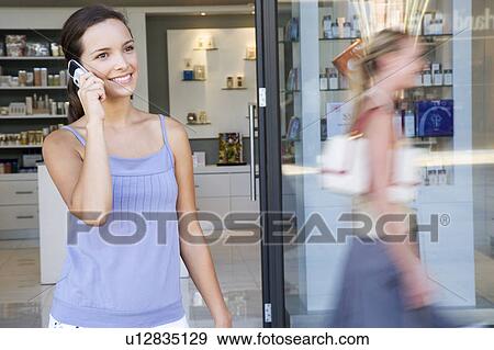 Woman leaving a shop, chatting on her mobile phone View Large Photo Image Stock Photo - Woman leaving a shop, chatting on her mobile phone. Fotosearch