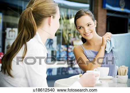 Woman showing clothes purchase to her friend over coffee at a pavement cafe View Large Photo Image Stock Image - Woman showing clothes purchase to her friend over coffee at a pavement cafe. Fotosearch
