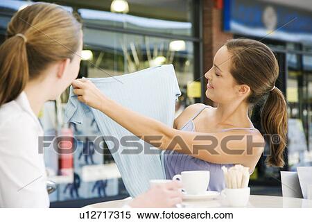 Woman showing clothes purchase to her friend over coffee at a pavement cafe View Large Photo Image Stock Photography - Woman showing clothes purchase to her friend over coffee at a pavement cafe. Fotosearch