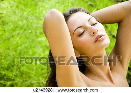 Stock Image - Beauty portrait of a woman in a tropical setting hands behind her head... Fotosearch