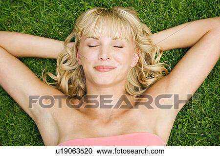 Stock Image - Beauty portrait of a woman laying in the grass in a tropical setting.. Fotosearch