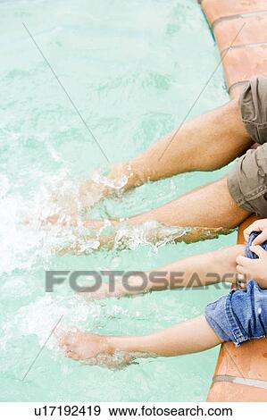 Stock Photo - cropped image man and boy's feet splashing in swimming pool. Fotosearch