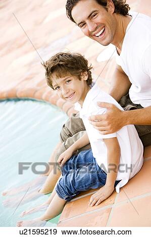 Stock Photo - father and son sitting on edge of swimming pool. Fotosearch