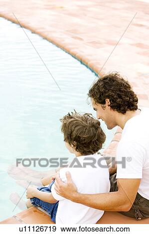 Stock Photo - father and son sitting on the edge of swimming pool. Fotosearch