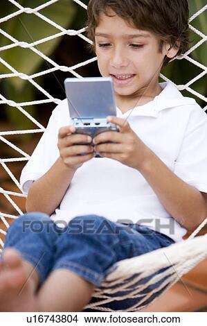 little boy playing electronic game sitting in hammock View Large Photo Image Picture - little boy playing electronic game sitting in hammock. Fotosearch