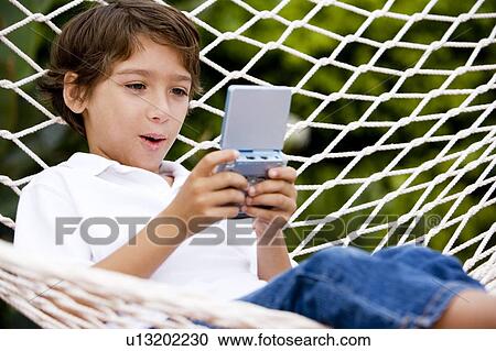 little boy playing electronic game sitting in hammock View Large Photo Image Stock Image - little boy playing electronic game sitting in hammock. Fotosearch