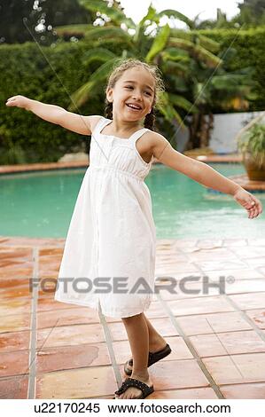 Stock Photography - little Hispanic girl dancing on terrace by pool. Fotosearch