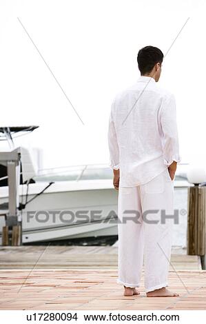 Picture - Man in white standing on a jetty by a boat. Fotosearch