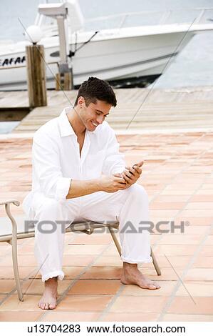 Man sitting by a boat in the harbour, using a mobile phone View Large Photo Image Stock Image - Man sitting by a boat in the harbour, using a mobile phone. Fotosearch
