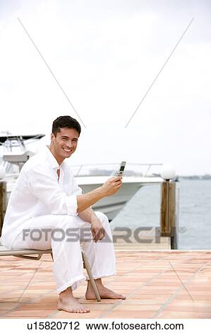 Man sitting by a boat in the harbour, using a mobile phone View Large Photo Image Stock Image - Man sitting by a boat in the harbour, using a mobile phone. Fotosearch