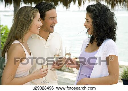 Stock Photograph - Three friends at a tropical hotel bar, having a drink. Fotosearch