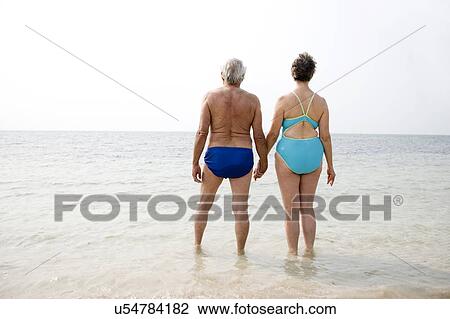Stock Image - Portrait of a senior couple hand in hand walking in the sea. Fotosearch