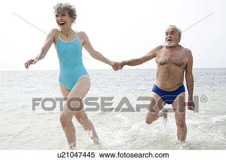 Stock Photography - Portrait of a senior couple hand in hand running in the sea. Fotosearch