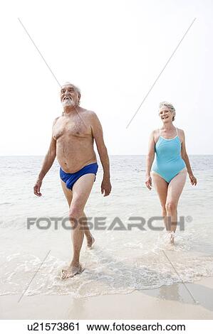 Stock Image - Portrait of a senior couple walking in the sea. Fotosearch