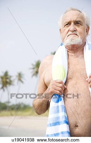 Stock Photo - Portrait of a senior man in a swimsuit and towel at the beach . Fotosearch