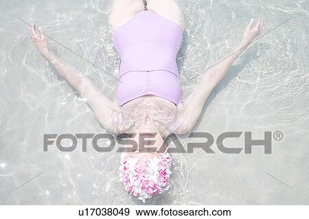 Stock Photo - Senior woman in a swimming hat, floating in the ocean . Fotosearch